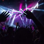 Public de concert vu de derrière, main levée, ambiance tamisée